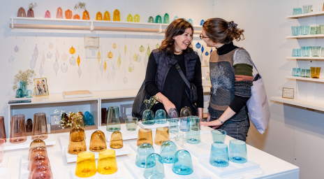 Two women shopping for homemade glass items at One Of A Kind Spring Show.